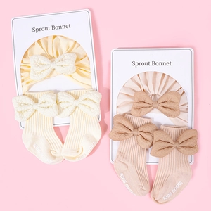 Detail of baby cotton bonnet and socks set with elegant ribbon bow in cream and tan colors