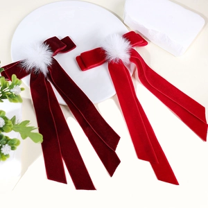 Detail of red velvet bow hair clip with plush white pompom and long streaming ribbons