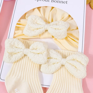 Creamy yellow cotton baby hat and socks set with a large textured decorative bow