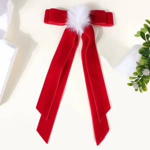 Detail of red velvet bow hair clip with white pom-pom and long ribbon tails
