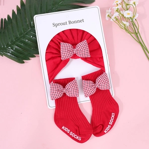 Detalle del gorro de bebé rojo y calcetines a juego con lazos de cuadros en fondo rosa