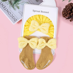 Detail of baby cotton hat and socks set with fluffy beige bows on a pink background