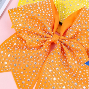 Close-up of orange rhinestone bow hair clip with grosgrain texture and elastic band