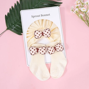 Detalle del set de gorro y calcetines para bebé en crema con lazos de lunares marrones