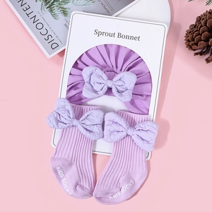 Flat lay of purple cotton baby bonnet and matching bow socks on pink background
