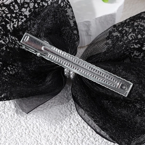 Detail of a black lace bow hair clip with white pearls and silver metal alligator clip