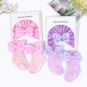 Pink and purple cotton baby hat and sock set with bows on a clean white background