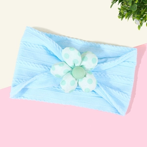 Détail du bandeau bébé en tricot bleu avec décoration de fleur blanche à pois verts