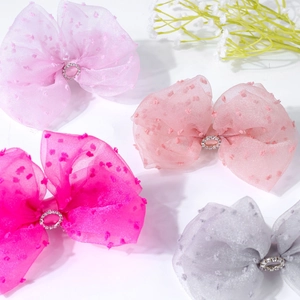 Close-up of four glitter bow hair clips in pink, purple, and gray with rhinestone centers