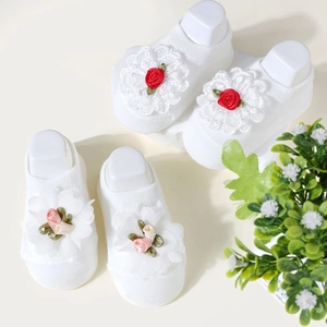Close-up of white baby knit socks with handmade red and pink floral lace decorations