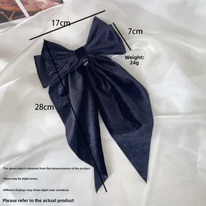 Detail shot of a large black velvet bow hair clip with long ribbon streamers on white satin