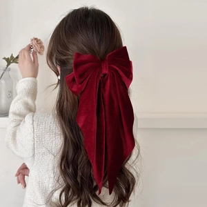 Detailed back view of a large burgundy velvet bow hair clip with long ribbons on wavy hair