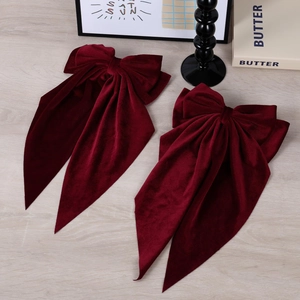 Macro detail of two burgundy velvet bow hair clips with long ribbons on wooden surface