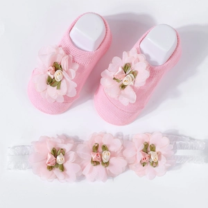 Detail of pink knitted baby booties with floral decor and a matching white lace headband
