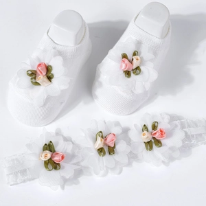 Detailed view of white knitted baby socks and matching headband with chiffon floral accents
