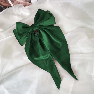Close-up of a large dark green satin bow hair clip with long ribbons on silk fabric