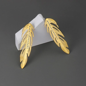 Boucles d'oreilles plume dorées avec zircons blancs brillants sur fond gris élégant