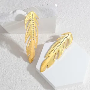 Boucles d'oreilles pendantes plumes dorées avec strass sur un support géométrique blanc