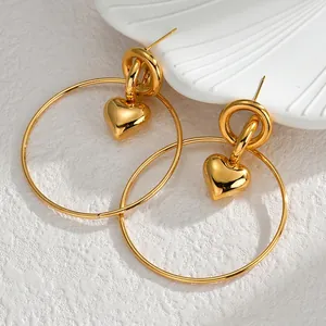 Grandes créoles dorées minimalistes avec pendentif cœur 3D sur fond de pierre blanche