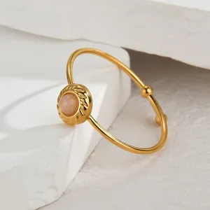 Close-up of pink cabochon gemstone ring with golden braided edge and asymmetrical beads