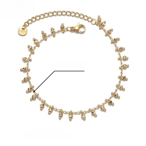 Close-up of gold 14K stainless steel tassel bracelet with bead charms and logo tag