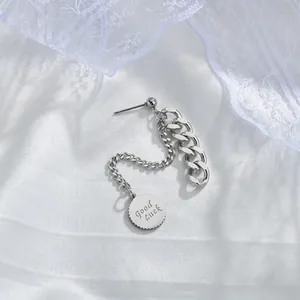 Minimalist stainless steel chain earring with a Good Luck pendant on white silk fabric