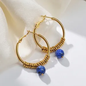 Boucles d'oreilles créoles dorées avec perles bleues sur fond de tissu en soie