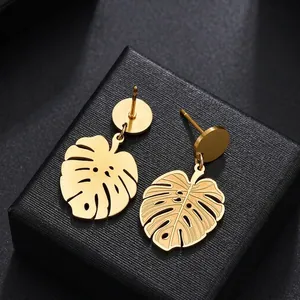 Vintage gold monstera leaf drop earrings in stainless steel on black textured background