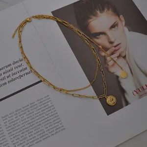 Collier double rang doré avec maillons plats et médaillon vintage posé sur un magazine