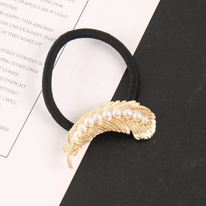 Detail of a black hair tie featuring a golden feather charm with inset white pearls