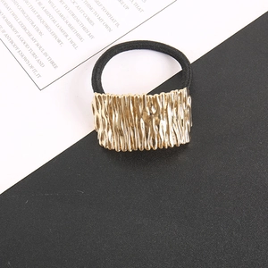 Detail of golden metal hair tie with irregular textured surface and black elastic band