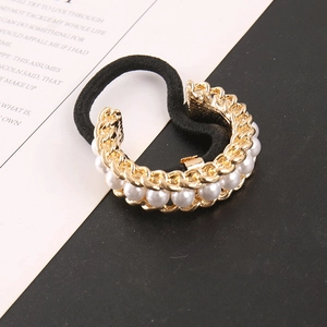 Detail of a vintage gold hair tie with chain texture and elegant white pearls on black band