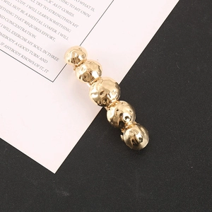 Close-up of golden ball hair clip with hammered metal texture on a white card