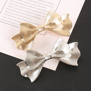 Close-up of gold and silver textured metal bow hair clips with satin finish on paper