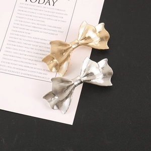 Close-up of gold and silver metal bow hair clips with industrial striped texture finish