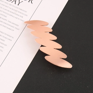 Dettaglio della molletta per capelli ondulata in oro rosa con trama metallica satinata