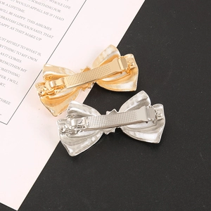 Close-up of gold and silver metallic bow hair clips with refined striped texture
