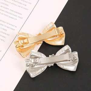 Detail of metal bow hair clips showing textured stripes and spring clip mechanism