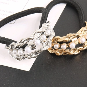 Detailed macro view of black elastic hair tie with pearl chain and gold metal accents