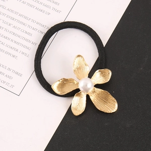 Detail eines goldenen Blumen-Haargummis mit weißer Perle und schwarzem elastischem Band