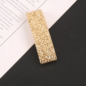Détail d'une pince à cheveux dorée rectangulaire à texture martelée sur page de livre