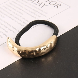 Close-up of golden crescent metal hair tie with textured hammered finish and black elastic