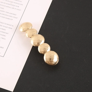 Detail of gold metal hair clip with wavy pleated texture on a modern split background