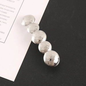 Detailed close-up of textured silver metal hair clip with five circular hammered plates