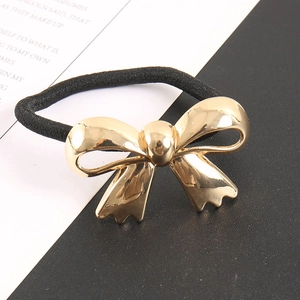 Elastic black hair tie with a polished gold bow pendant on a minimalist background