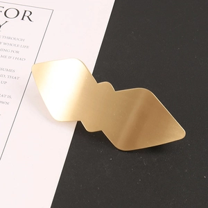 Détail macro d'une pince à cheveux géométrique en or mat sur fond bicolore moderne