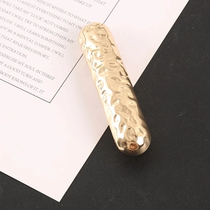 Detail of minimalist gold-tone alloy hairclip featuring a unique hammered metal texture