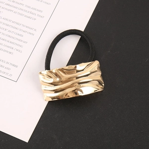 Detail of a minimalist gold textured rectangular alloy hair tie with black elastic band