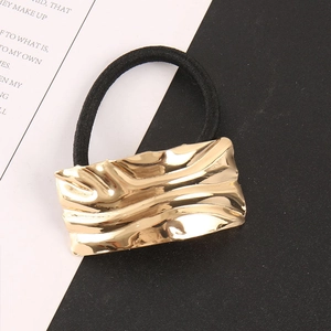 Close-up of golden rectangular corrugated metal charm on a black high-elastic hair tie