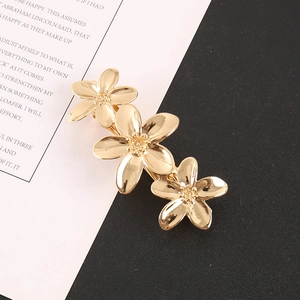 Détail d'une pince à cheveux en métal doré ornée de trois fleurs à cinq pétales
